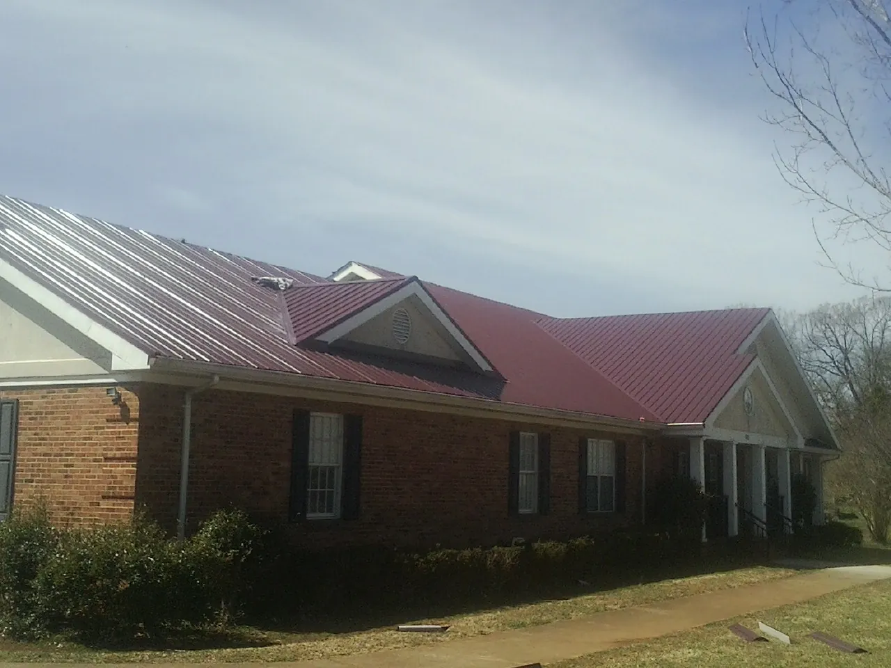 Red metal roof with gabled entries on a long brick building, from a Hail Damage Roof Repair job in Cameron