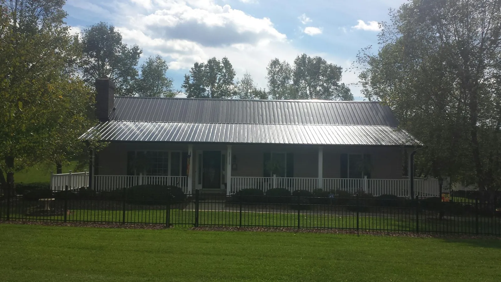Gray metal roof on a brick ranch with a full width front porch — Gutter Guard Installation work by our crew in Cameron